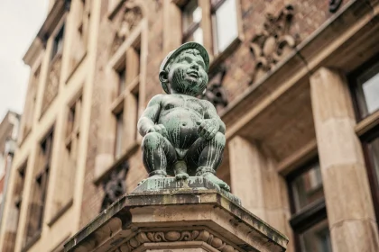 Statue du Manneken-Pis en bronze patiné vert à Bruxelles, photographiée en contre-plongée avec la façade flamande en arrière-plan
